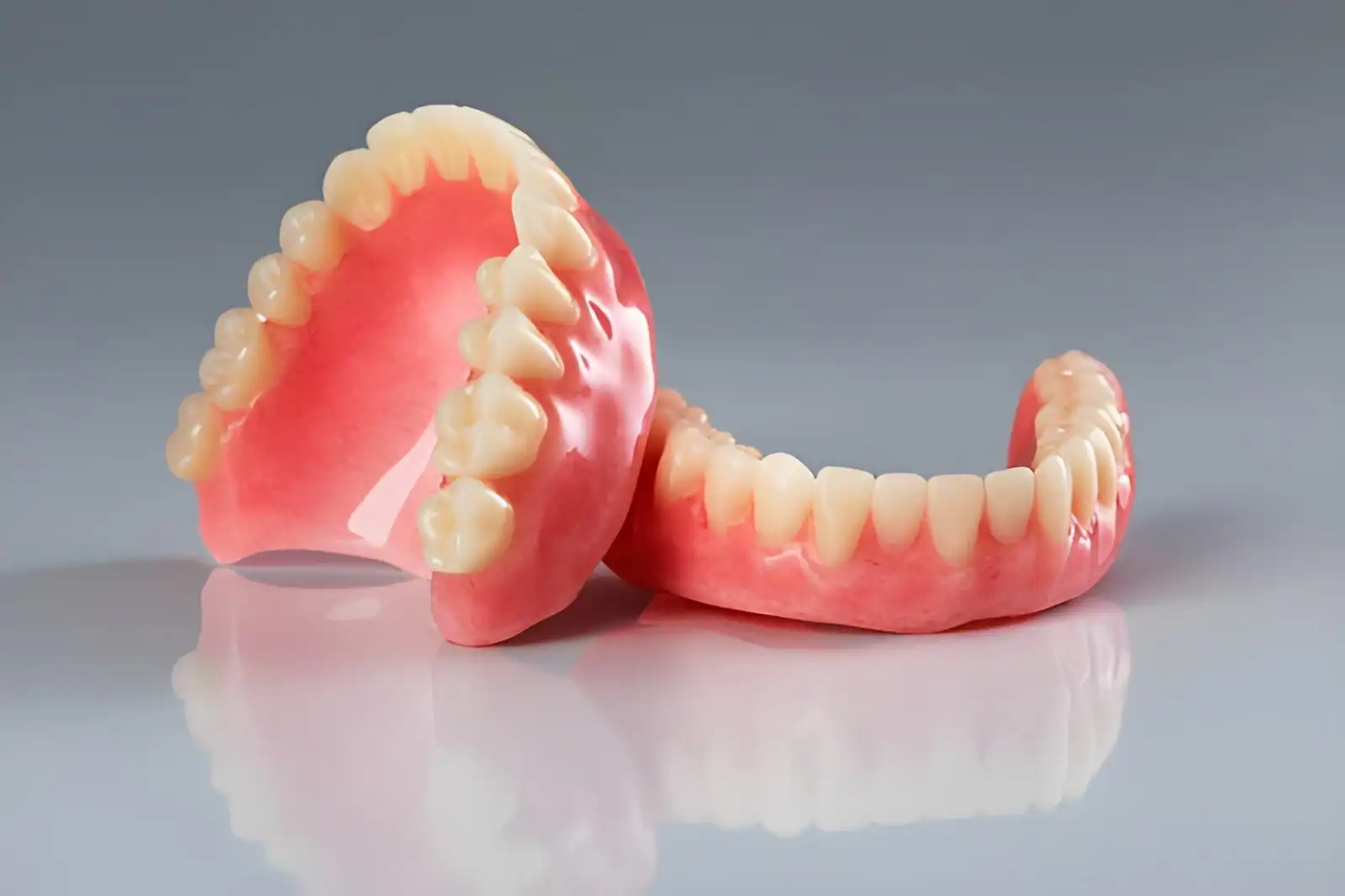 Full upper and lower dentures displayed on a reflective dental surface